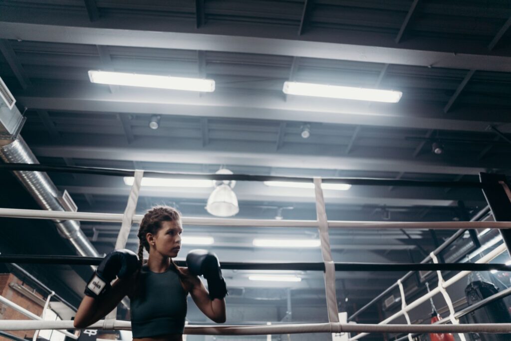 Boxeuse en garde, seule au milieu du ring, sous les lumières de la salle