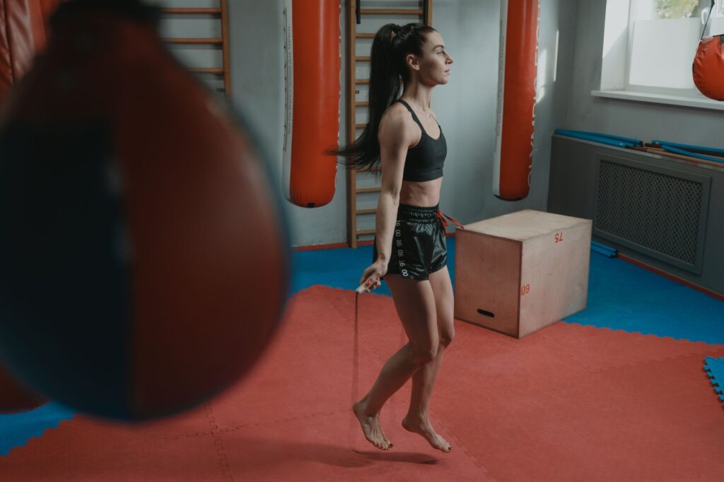 Pratiquante qui saute à la corde dans une salle de boxe, entourée de sacs de frappe