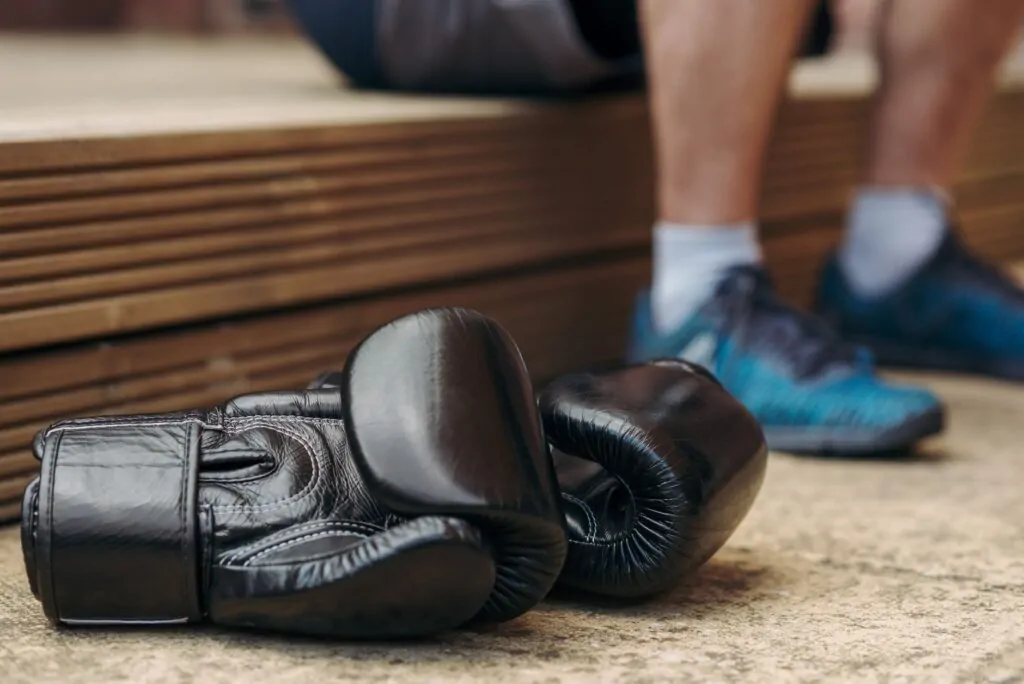 Paire de gants de boxe noirs posée au sol, un pratiquant assis derrière