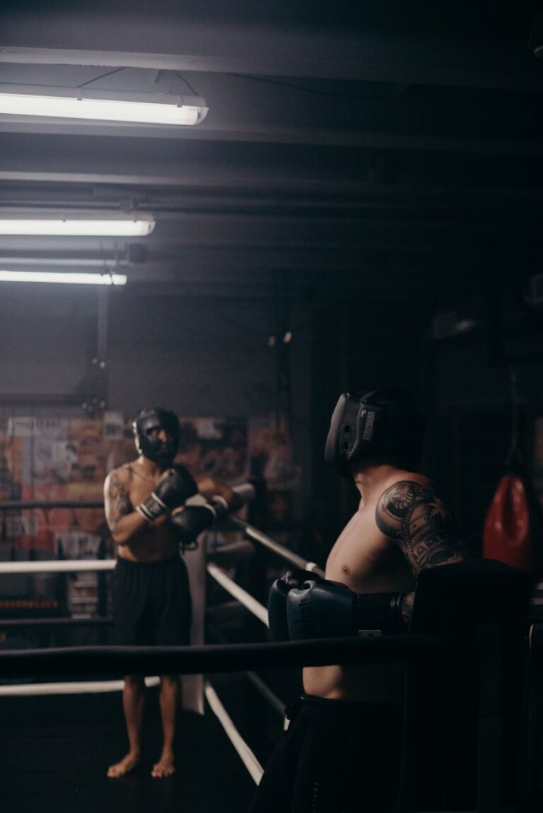 Deux boxeurs casqués face à face sur un ring, dans une salle sombre